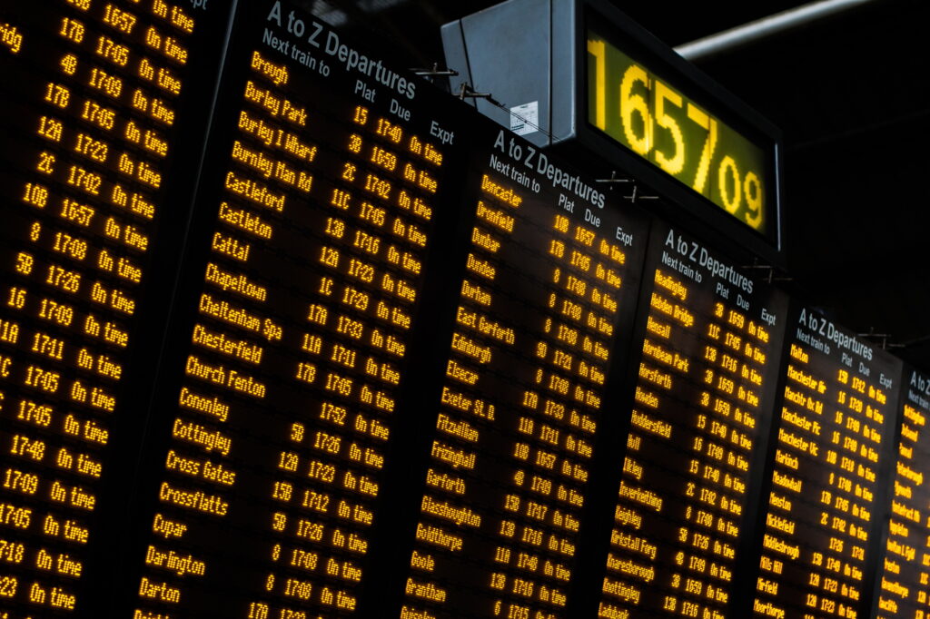 An electronic train station information board and clock Showing departure arrival times and delays