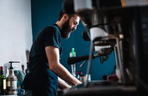 Barista preparing cappuccino on espresso machine for customer in coffee shop.