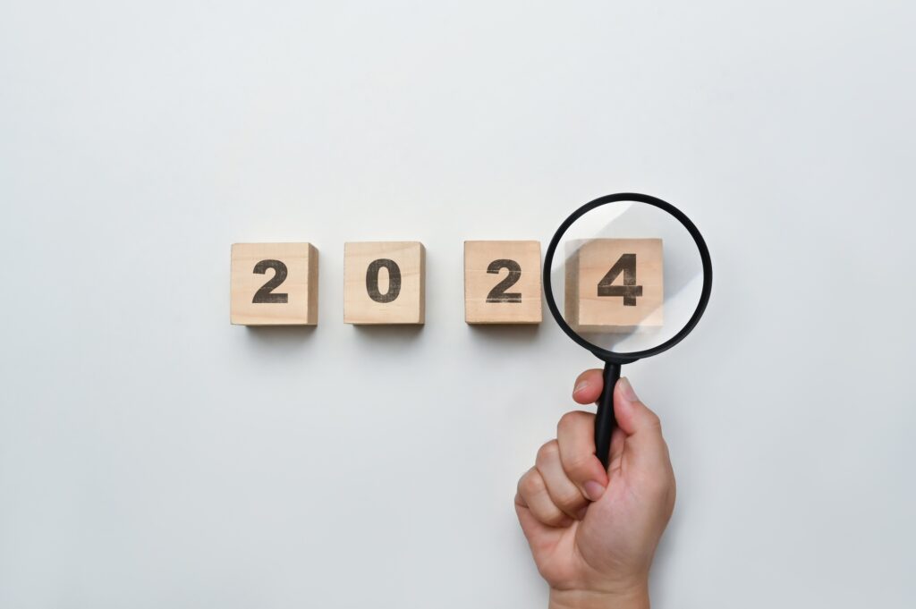 Magnifying glass and wooden cubes with 2024 year number on white background.