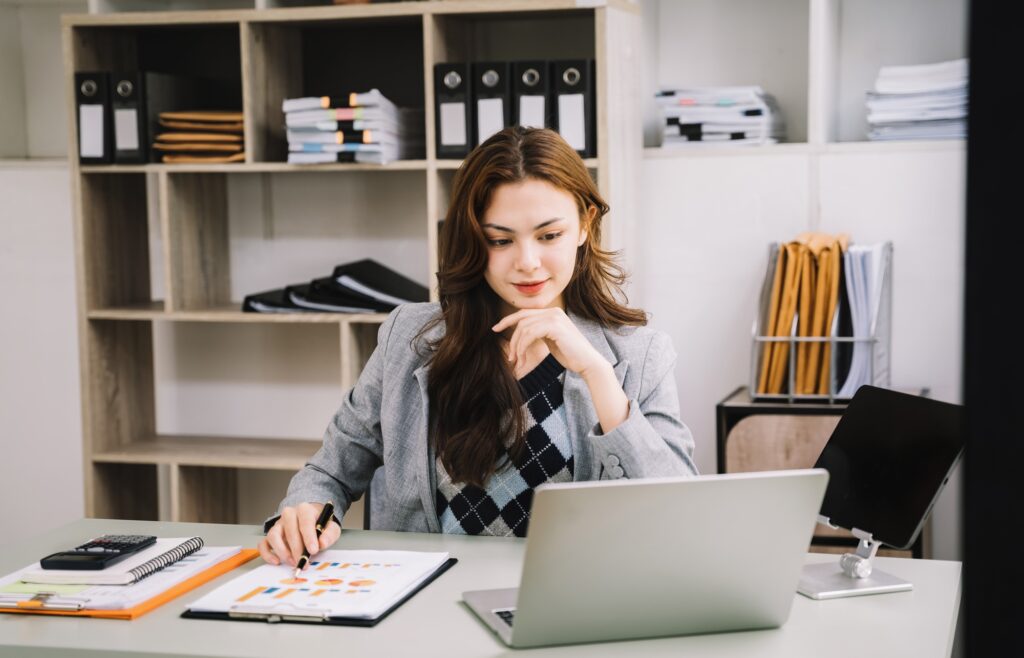 Portrait of Asian businesswoman working on laptop and papers on table in her office.