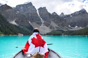 Young girl wrapped in a Canadian flag riding in a canoe on turquoise lake surrounded by mountains