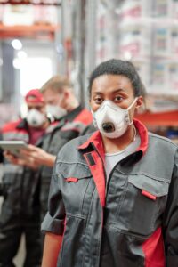 Young mixed-race woman in workwear and respirator standing in front of camera